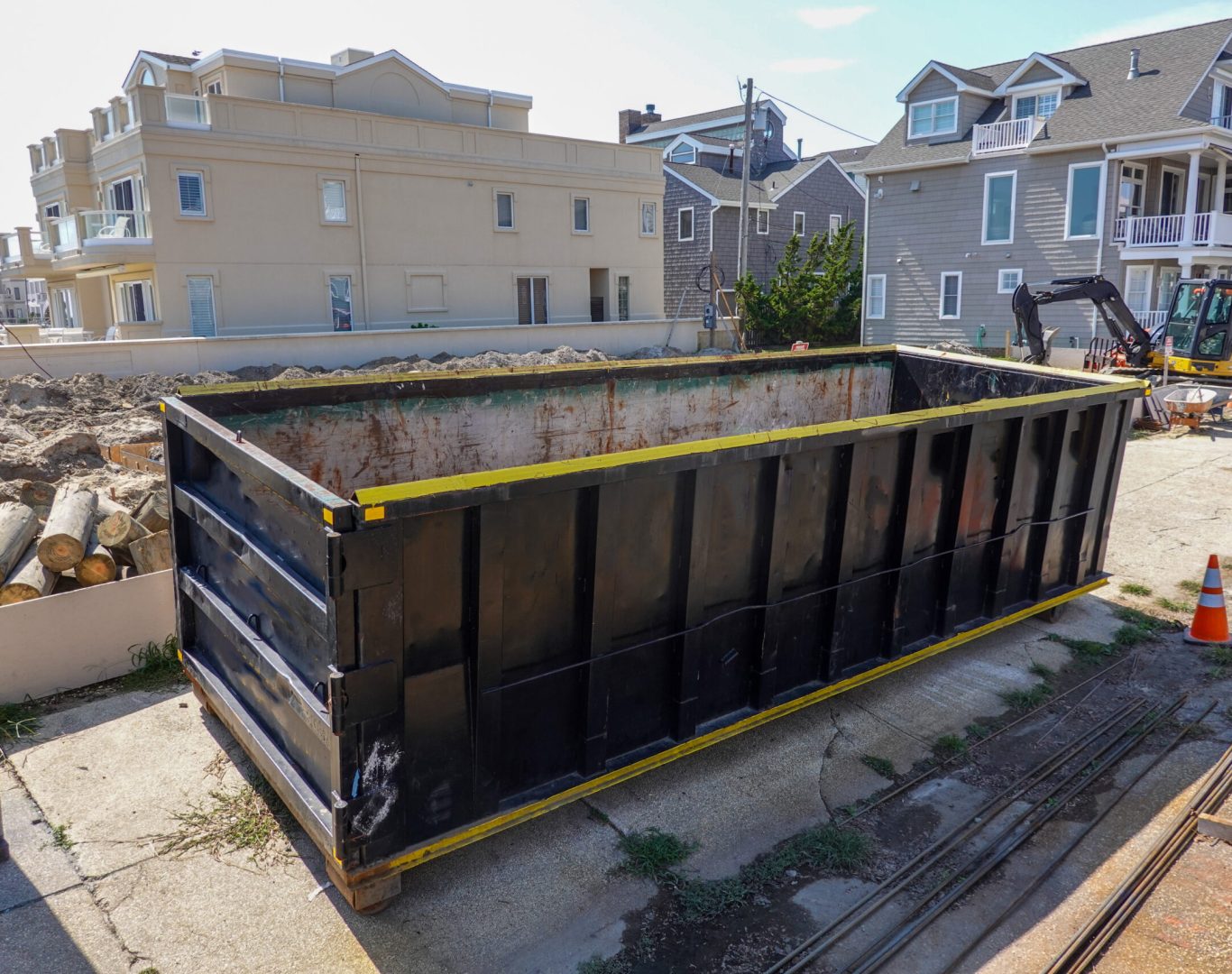 An empty black dumpster is seen at a construction site near a backhoe